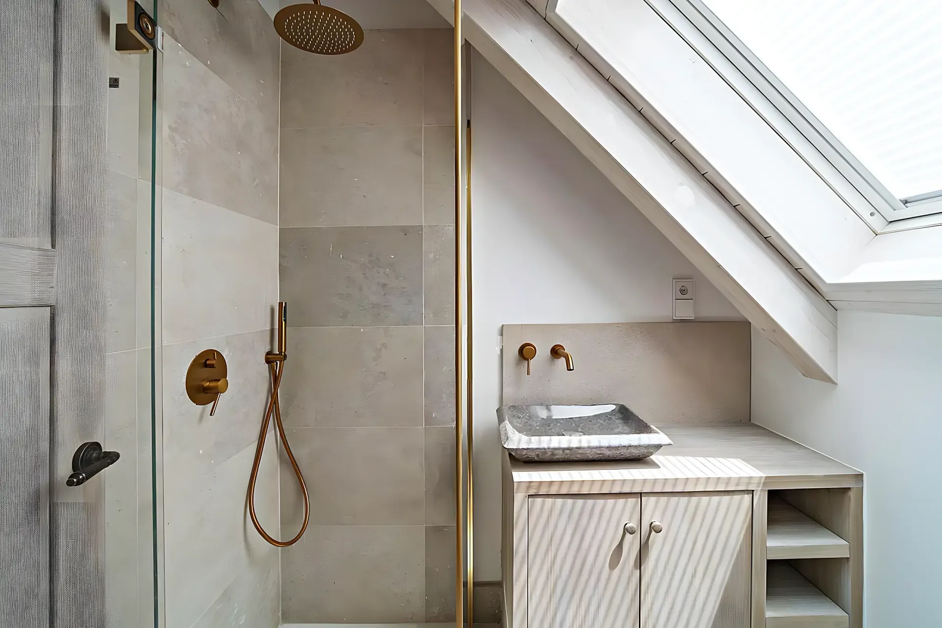 Salle de bain mansardée avec douche en pierre, robinetterie dorée et puits de lumière