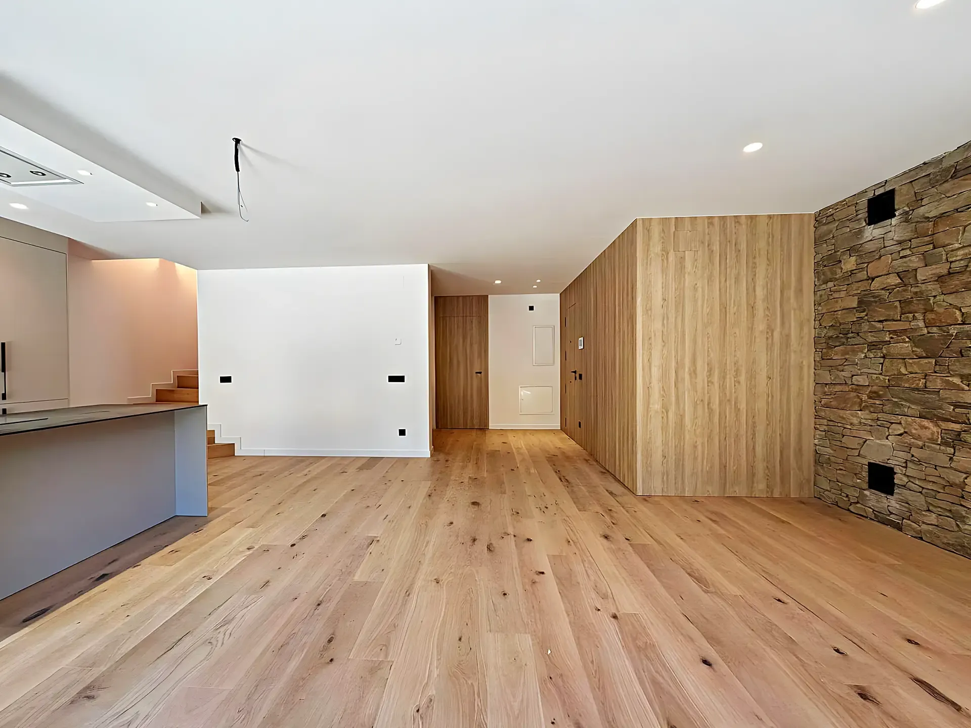 Interior amb paret de pedra vista, revestiment de roure i cuina fosca al fons
